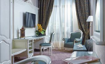 a luxurious living room with a large window , blue chairs , and a flat - screen tv on the wall at Savoy Hotel