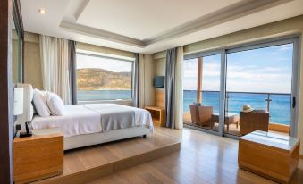 a modern hotel room with a large bed , wooden flooring , and sliding glass doors that offer a view of the ocean at Konstantinos Palace