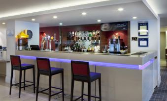 a modern bar with a long counter , multiple stools , and various liquor bottles on display at Holiday Inn Express Milton Keynes