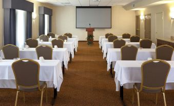 a conference room with white tablecloths and chairs , a projector screen , and a man standing at the front at Country Inn & Suites by Radisson, Rocky Mount, NC