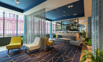 a modern lounge area with blue and yellow furniture , a large window , and geometric patterns on the floor at Hampton by Hilton Antwerp Central Station