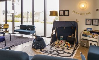a living room with a blue couch , a dining table , and a play tent in the corner at Ibis Styles Paris Romainville