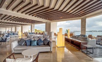 a modern , open - concept living room with wooden floors and a view of the ocean , featuring comfortable seating arrangements and a bar area at Royalton Negril, An Autograph Collection All-Inclusive Resort