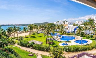 a beautiful resort with a large pool surrounded by lush greenery , including palm trees , grass , and bushes at Camino Real Zaashila Huatulco