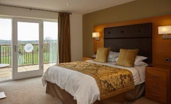 a large bed with a brown headboard and white sheets is in a room with a sliding glass door at Hundith Hill Hotel