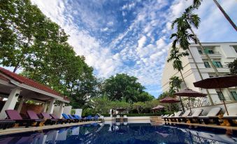 a large outdoor swimming pool surrounded by lounge chairs and umbrellas , with trees in the background at Tara Angkor Hotel
