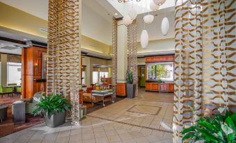 a large , modern hotel lobby with wooden columns and hanging lights , surrounded by various seating arrangements at Hilton Garden Inn Kankakee