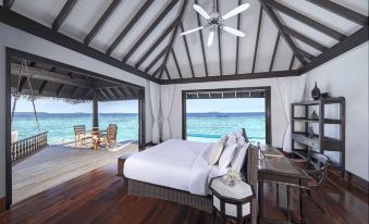 a bedroom with a bed , ceiling fan , and sliding glass doors leading to an ocean view at Anantara Kihavah Maldives Villas