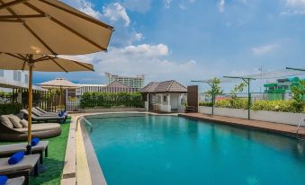 a large swimming pool with a lounge area and umbrellas , surrounded by trees and buildings at Rattanachol Hotel