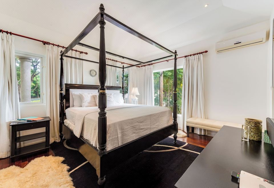 a modern bedroom with a black four - poster bed , white bedding , and a black rug on the floor at The Palms Resort