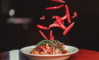 a white bowl filled with noodles and red chili peppers is being splashed by a green plant at Holiday Inn Beach Resort