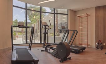 a well - equipped gym with various exercise equipment , such as treadmills , ellipticals , and stationary bikes , arranged in front of a window at JL Hotel by Bourbon