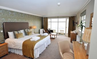 a large bed with white linens and a brown blanket is in a room with a desk , chairs , and a window at Beech Hill Hotel & Spa