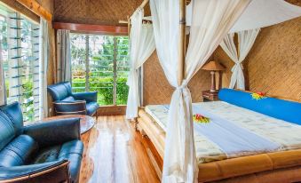 a bedroom with a large bed and white canopy curtains , surrounded by wooden walls and hardwood floors at Maravu Taveuni Lodge