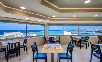 a restaurant with blue chairs and tables , a large window offering a view of the ocean , and a dining area with white plates and glasses at Marin Hotel