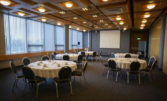 a large conference room with multiple round tables and chairs , a screen at the front , and windows on one side at Hotel Selfoss
