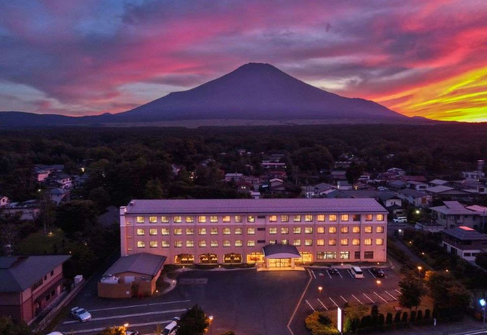 a large hotel with a mountain in the background and a pink and orange sunset in the foreground at Fuji Matsuzono Hotel