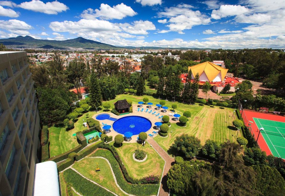 a bird 's eye view of a resort with a large pool surrounded by lush greenery and a city in the background at Best Western Plus Gran Hotel Morelia