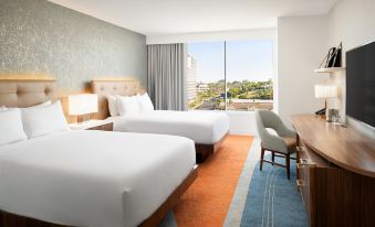 a hotel room with two beds , a window offering a view of the city , and a small desk at Hilton Los Angeles-Culver City, CA
