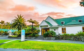 a beautiful white house with a green roof , surrounded by lush tropical plants and trees , set against a backdrop of a sunset sky at Scenic Hotel Bay of Islands