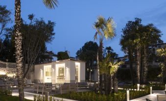 a modern white building with large windows , surrounded by palm trees and lit up at night at Palazzo Castri 1874 Hotel & Spa