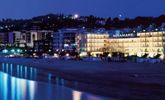 a beach scene at night , with a tall building in the background and lights illuminating the area at Hotel Miramare