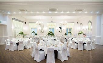 a large , white - walled room with multiple tables set for a formal event , decorated with green plants and chandeliers at Cbh Hythe Imperial Hotel Golf and Spa