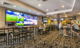 a well - lit bar area with various chairs and tables , as well as a large screen tv mounted on the wall at Nightcap at Waltzing Matilda Hotel