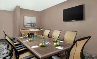 a conference room with a wooden table , chairs , and a television mounted on the wall at Home2 Suites by Hilton Long Island Brookhaven