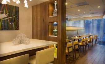 a modern restaurant with wooden tables and chairs , a bar area , and a large window at Aloft Miami Dadeland