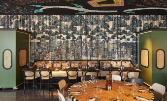 a restaurant with a large dining table surrounded by chairs , and a mural on the wall at Mama Shelter Lille