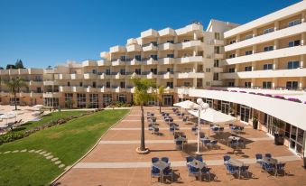 a large white building with multiple balconies and umbrellas , surrounded by an open courtyard with tables and chairs at Vila Gale Nautico