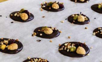 a tray filled with dark chocolate candies topped with nuts and seeds is placed on a white background at Ibis Lagos Ikeja