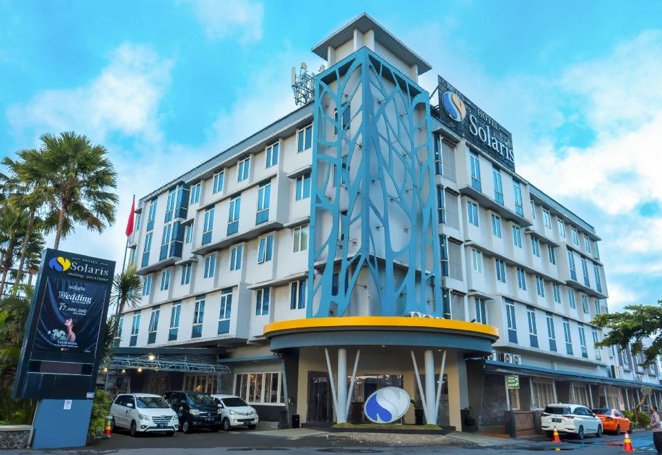 a large building with a blue and yellow geometric design is surrounded by cars and trees at Solaris Hotel Malang