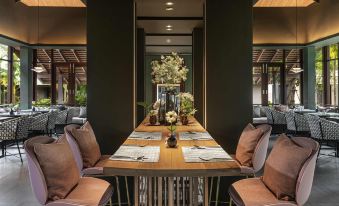 a long wooden table with chairs and a vase of flowers in the center is set for an elegant dining experience at Grand Mercure Khao Lak Bangsak