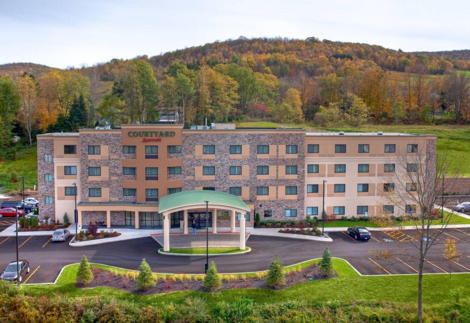 a large hotel with a green roof and a canopy is situated in front of a mountain at Courtyard Oneonta Cooperstown Area