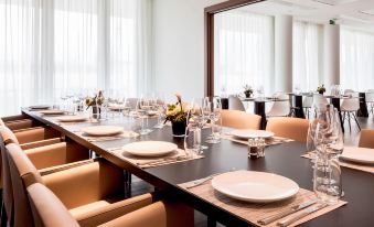 a large dining room with a long wooden table set for a meal , surrounded by chairs at AC Hotel Paris le Bourget Airport
