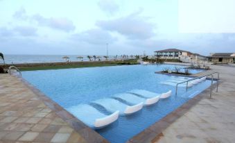 a large swimming pool with blue water and white lounge chairs is surrounded by a beach house at Serena Beach Resort