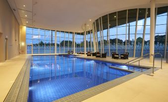 a modern swimming pool area with large windows , surrounded by comfortable seating and facilities , under the glow of evening lights at Hilton at St.George's Park, Burton Upon Trent