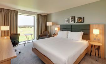 a large bed with white linens is in a room with a chair , lamp , and desk at Hilton Garden Inn Doncaster Racecourse