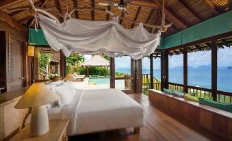 a large bed with white linens is in a room with wooden floors and walls , overlooking a pool and the ocean at Six Senses YAO Noi