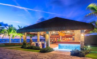 a modern building with a thatched roof , surrounded by palm trees and other greenery , illuminated by lights against the night sky at Hotel Village Porto de Galinhas