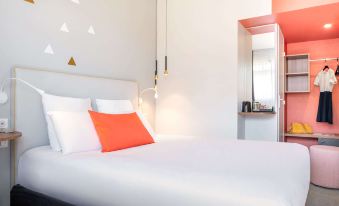 a white bed with an orange pillow and a mirror on the wall , creating a modern bedroom atmosphere at Kyriad Lyon Est - Saint Quentin Fallavier