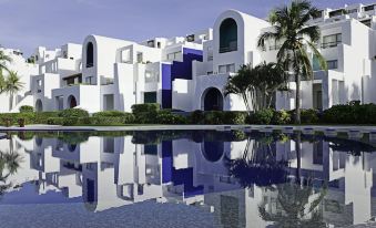 a white building with blue accents is reflected in the water of a pool below at Camino Real Zaashila Huatulco