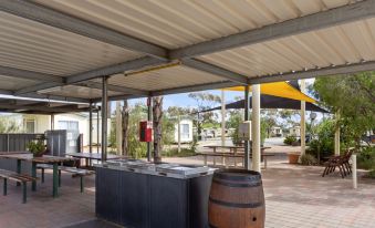 an outdoor dining area with a covered patio , tables , chairs , and a fire pit , surrounded by trees at Broken Hill Tourist Park