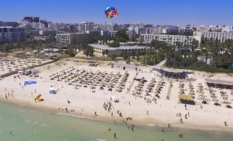 aerial view of a sandy beach with people and umbrellas , surrounded by buildings and palm trees at Hotel Marhaba Beach