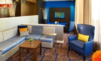 a modern living room with blue walls , wooden furniture , and an orange accent chair , along with a bar area in the background at Courtyard Detroit Dearborn