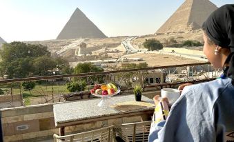a woman standing on a balcony overlooking the great pyramids of giza , egypt , and holding a cup of coffee at Pyramids View Inn