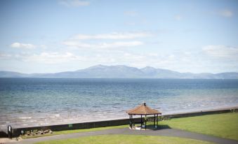 a grassy field near a body of water , with a gazebo and a bench placed near the water 's edge at Seamill Hydro Hotel