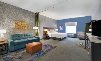 a hotel room with a blue couch , bed , and desk , as well as a desk , chair , and window at Home2 Suites by Hilton Lawrenceville Atlanta Sugarloaf